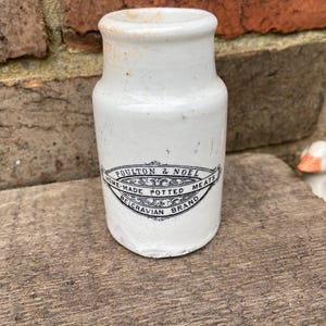 May include: White ceramic jar with a black and white label that reads "Poultons & Noel Home-Made Potted Meats Belgravian Brand".