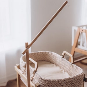May include: A wooden stand with a beige woven bassinet, a wooden arm with a hook at the end, and a pillow with a red and white mushroom design.