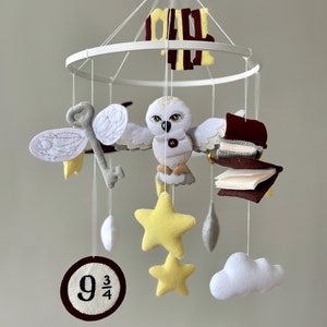May include: A white owl, yellow stars, a book, and a cloud mobile with a white and gray key and a 9 3/4 circle. The mobile is hanging from a white metal ring.