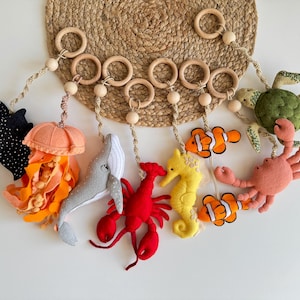 May include: A colorful felt ocean-themed baby mobile with a whale, jellyfish, seahorse, lobster, crab, and two clownfish hanging from wooden rings.