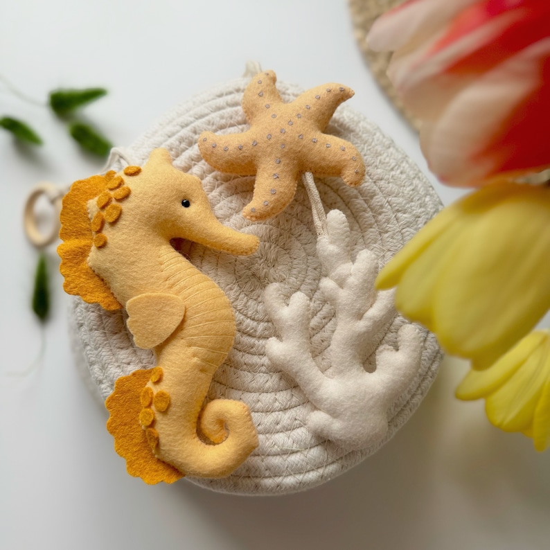 May include: A felt seahorse, starfish, and coral reef set in shades of yellow and cream. The seahorse has a yellow body with orange accents. The starfish is light yellow with small gray dots. The coral is white.
