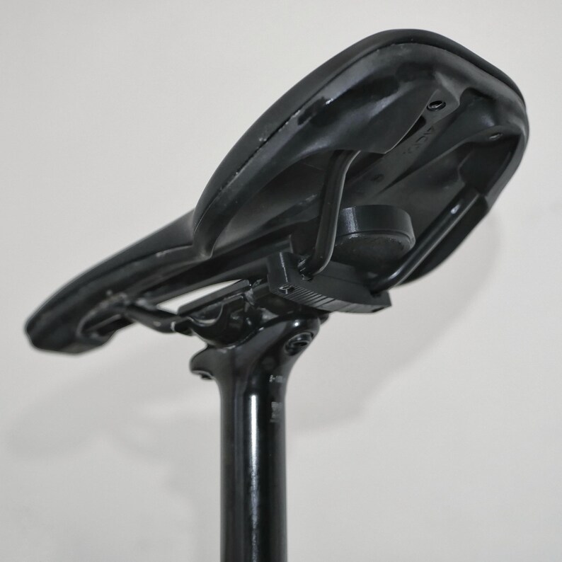 K&ouml;nnte beinhalten: Schwarzer Fahrradsattel mit einer schwarzen Sattelst&uuml;tze. Der Sattel ist mit einer Metallklemme an der St&uuml;tze befestigt.