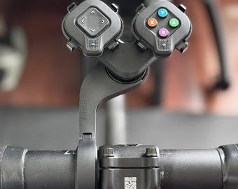 May include: Black Garmin bike handlebar remote with two control units. One unit has directional arrows, and the other has colored buttons. The remote is mounted on a black handlebar with a Shimano stem.