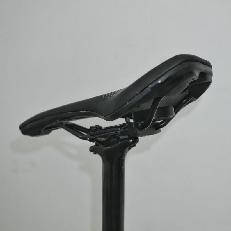 K&ouml;nnte beinhalten: Ein schwarzer Fahrradsattel mit einem geschwungenen Design und einer schwarzen Sattelst&uuml;tze.