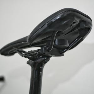 K&ouml;nnte beinhalten: Schwarzer Fahrradsattel mit einer schwarzen Metallhalterung, die an der Sattelst&uuml;tze befestigt ist.