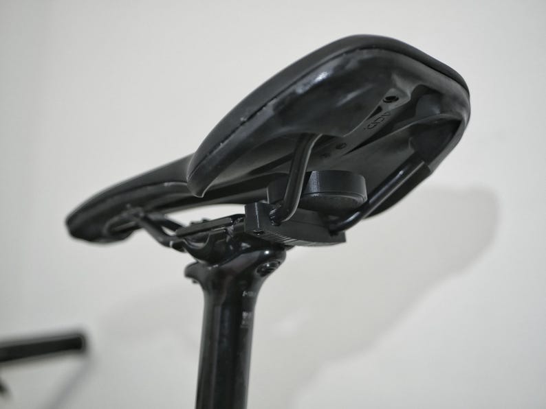K&ouml;nnte beinhalten: Schwarzer Fahrradsattel mit einer schwarzen Metallhalterung, die an der Sattelst&uuml;tze befestigt ist.