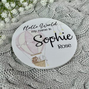 May include: A white round wooden sign with the text "Hello World my name is Sophie Rose" and a pink and white hot air balloon with a teddy bear and bunny rabbit in the basket.