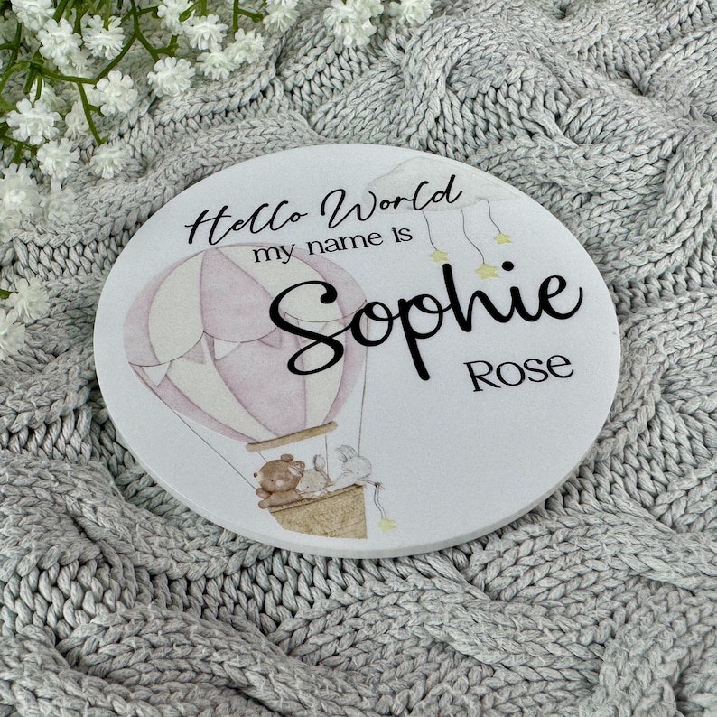 May include: A white round wooden sign with the text "Hello World my name is Sophie Rose" and a pink and white hot air balloon with a teddy bear and bunny rabbit in the basket.