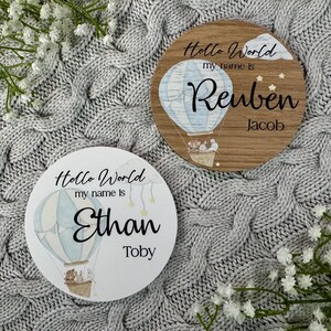 May include: Two round wooden signs with a hot air balloon design. The signs say "Hello World, my name is" and include a name and a second name. The first sign says "Reuben Jacob" and the second sign says "Ethan Toby".