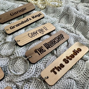 May include: A set of six wooden keyrings with different engraved text, including "Garage", "Granddad's Keys", "George H", "The Workshop", "The Studio", and "Door". Each keyring has a silver metal ring.