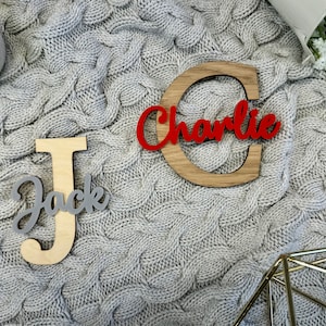 May include: Wooden name cutouts, featuring the names "Jack" and "Charlie". The name "Jack" is in a gray script font on a light wood letter "J". The name "Charlie" is in a red script font on a wooden letter "C".