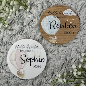 May include: Two round wooden signs with a hot air balloon design. The top sign says "Hello World my name is Reuben Jacob" and the bottom sign says "Hello World my name is Sophie Rose".