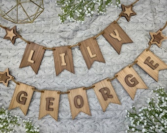 May include: Wooden banner with the names "Lily" and "George" spelled out in individual flags. Each letter is cut out of the wood and the flags are strung together with twine. There are stars on either end of the banner.