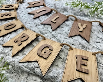 May include: Wooden banner with the name "GEORGE" spelled out in individual letters. Each letter is cut out of wood and attached to a brown wooden flag. The flags are connected by twine.