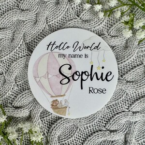 May include: A white round sign with the text "Hello World my name is Sophie Rose" and a pink and white hot air balloon with two animals in the basket.