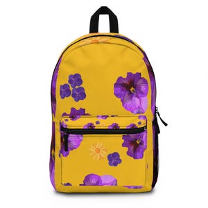 Puede incluir: Mochila amarilla con un estampado floral con pensamientos morados y rosados y margaritas amarillas.