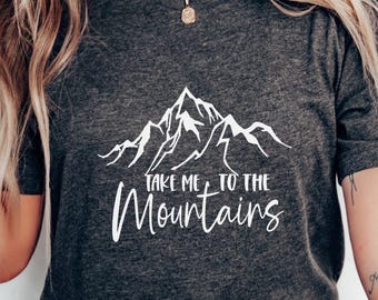 Op de afbeelding: Donkergrijs T-shirt met een witte bergafbeelding en de tekst "Take Me to the Mountains". Het shirt heeft een V-hals en korte mouwen. Het ontwerp is eenvoudig en strak, perfect voor buitenliefhebbers.