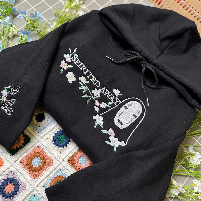 Pode incluir: Moletom preto com design floral e de personagem bordado. O design inclui o texto "SPIRITED AWAY" e um rosto de personagem. As mangas t&ecirc;m bordados florais. O moletom tem um capuz com cord&atilde;o.