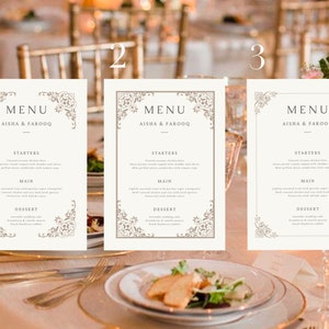 May include: Three white wedding menu cards with a decorative border and the text "MENU AISHA & FAROOQ" at the top. The cards are laid out on a table with a white tablecloth and gold cutlery.
