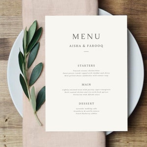 May include: A white menu card with the text "MENU" in a minimalist font. The names "AISHA & FAROOQ" are printed below the menu title. The menu lists starters, main courses, and desserts.