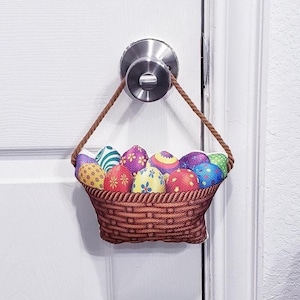 May include: A brown wicker basket filled with colorful Easter eggs hangs from a door knob. The basket is made of fabric and has a rope handle.