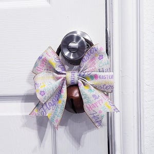 May include: A white door with a silver door knob and a bow made of fabric with the words "Happy Easter" printed on it.
