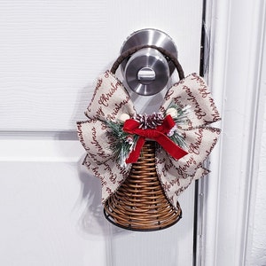 May include: A wicker bell with a red and white ribbon with the text "Merry Christmas" on it. The bell is hanging on a door knob.