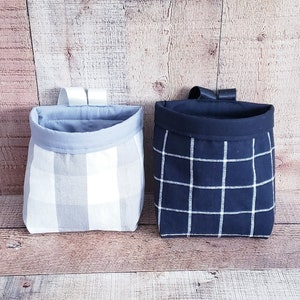 Könnte beinhalten: Zwei Stoffaufbewahrungskörbe mit Aufhängeschlaufen. Der Korb links ist in weiß-blauem Gingham. Der Korb rechts ist in schwarz-weißem Gingham.