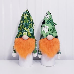 May include: Two gnomes with orange beards and green hats with shamrock patterns. The gnomes are wearing green and white plaid shirts.