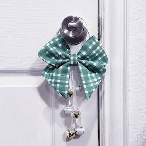 May include: A green and white checkered bow with a white ribbon and gold bells hanging from a door knob.