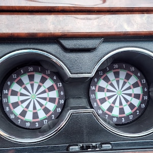 Könnte beinhalten: Zwei schwarze und silberne Dartboardhalter mit einem Dartboard in jedem. Die Dartboards sind schwarz und weiß mit einem roten und grünen Bullseye.