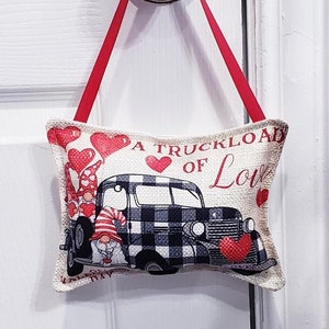 May include: A white door with a silver door knob. A red ribbon is tied around the knob and a small pillow with a black and white checkered truck and gnomes is hanging from the ribbon. The pillow has the text "A Truckload of Love" printed on it.