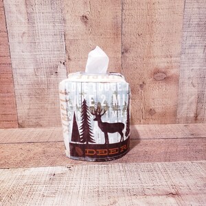 Op de afbeelding: Een witte tissueboxhoes met een bosontwerp. Het ontwerp bevat een hert, bomen en de tekst "DEER" en "LOVE TO GOGE LAKE 2 MI 1 MILE".