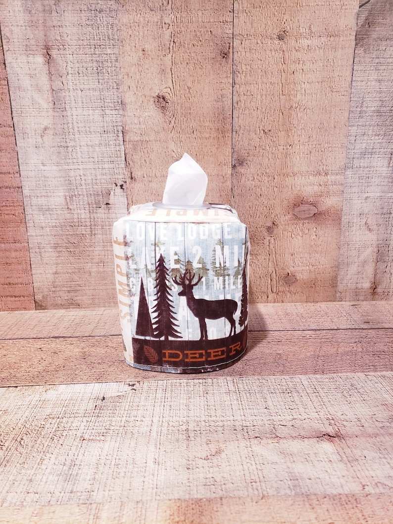 Op de afbeelding: Een witte tissueboxhoes met een bosontwerp. Het ontwerp bevat een hert, bomen en de tekst "DEER" en "LOVE TO GOGE LAKE 2 MI 1 MILE".