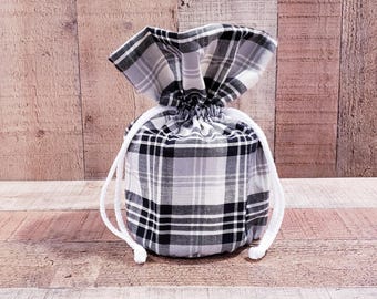 May include: A black and white plaid drawstring bag with white drawstrings. The bag is made of fabric and is sitting on a wooden surface.