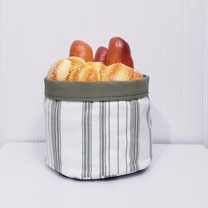 May include: A white and green striped fabric bread basket with a green fabric top. The basket is filled with bread rolls and loaves.