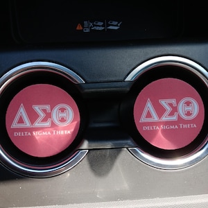 May include: Two pink car cup holders with the white letters "ΔΣΘ" and the words "Delta Sigma Theta" printed on them.