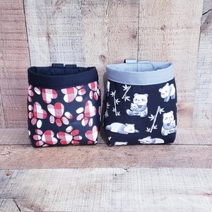May include: Two black fabric drawstring bags with different patterns. One bag has a red and white paw print pattern. The other bag has a black and white panda bear pattern.