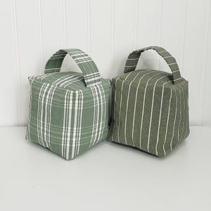 May include: Two green doorstops with handles. One is a plaid pattern and the other is a striped pattern.