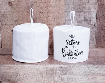 May include: Two white toilet paper roll covers. One cover has the text "No Selfies in the Bathroom Please" printed on it.