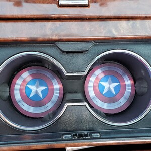 May include: Two round, red, white, and blue cup holders with a star in the center. The cup holders are in a car's cup holder compartment.