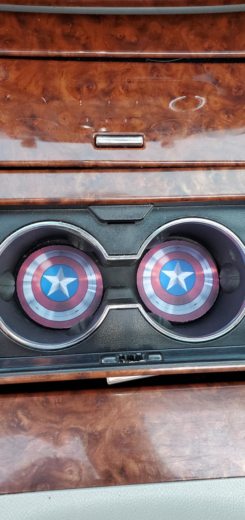 May include: Two round, red, white, and blue cup holders with a star in the center. The cup holders are in a car's cup holder compartment.