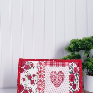 Puede incluir: Un bloque de colcha de retazos rojo, blanco y rosa con un gran coraz&oacute;n rojo en el centro. El coraz&oacute;n tiene un dise&ntilde;o blanco e intrincado. El bloque est&aacute; enmarcado con un borde rojo y tiene peque&ntilde;os corazones rosas en el borde.