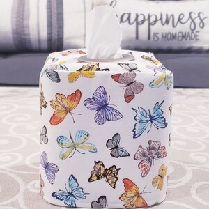 Pu&ograve; includere: Copertura per scatola di fazzoletti di carta bianca con un motivo di farfalle colorate. Il coperchio ha un fazzoletto di carta bianco che sporge dalla parte superiore.
