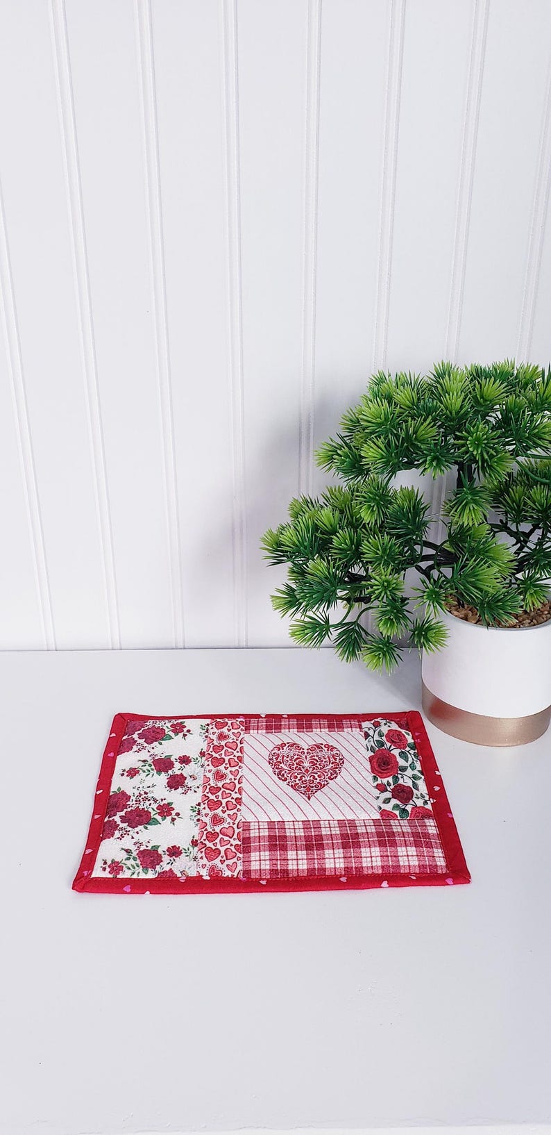 Puede incluir: Un posavasos de tela de patchwork rojo y blanco con un dise&ntilde;o de coraz&oacute;n en el centro. El posavasos est&aacute; rodeado por un borde rojo con peque&ntilde;os corazones rosas.