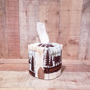 Op de afbeelding: Een bruine en witte tissueboxhoes met een bosontwerp met bomen, een beer en het woord "Beer".