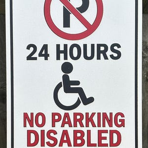 Könnte beinhalten: Weißes rechteckiges Schild mit schwarzem und rotem Text und Symbolen. Das Schild lautet "24 STUNDEN" und "KEIN PARKPLATZ BEHINDERTE PERSON". Ein roter Kreis mit einem durchgestrichenen schwarzen "P" und ein Rollstuhlsymbol sind ebenfalls vorhanden.