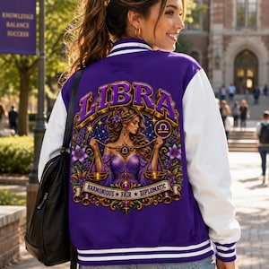 Könnte beinhalten: Eine violett-weiße Collegejacke mit einer großen Grafik auf der Rückseite, die eine Frau mit Waagschalen zeigt, umgeben von Blumen und dem Text LIBRA, HARMONIOUS, FAIR, DIPLOMATIC. Die Jacke hat weiße Ärmel, einen violetten Körper und gestreifte Rippbündchen.