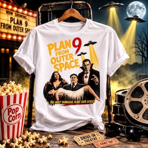 May include: A white t-shirt featuring a graphic print of the movie poster for Plan 9 from Outer Space. The design includes the film title in yellow and red text, illustrations of characters, flying saucers with light beams, and the tagline The Most Diabolical Plane Ever Devised.
