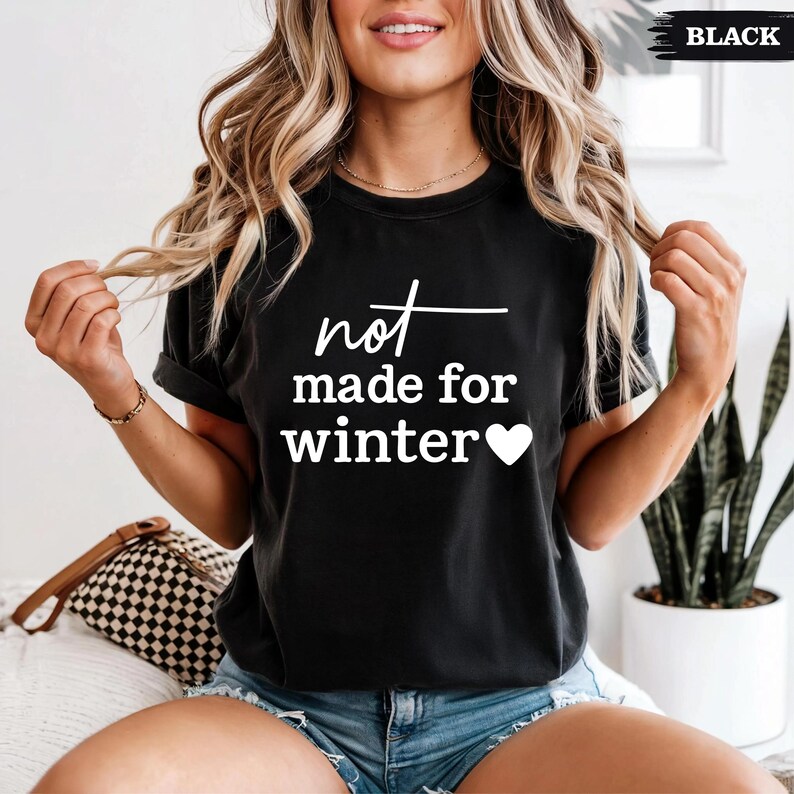 Puede incluir: Camiseta negra con el texto blanco "not made for winter" y un s&iacute;mbolo de coraz&oacute;n. La camiseta tiene mangas cortas y cuello redondo. La modelo lleva pantalones cortos vaqueros azules.